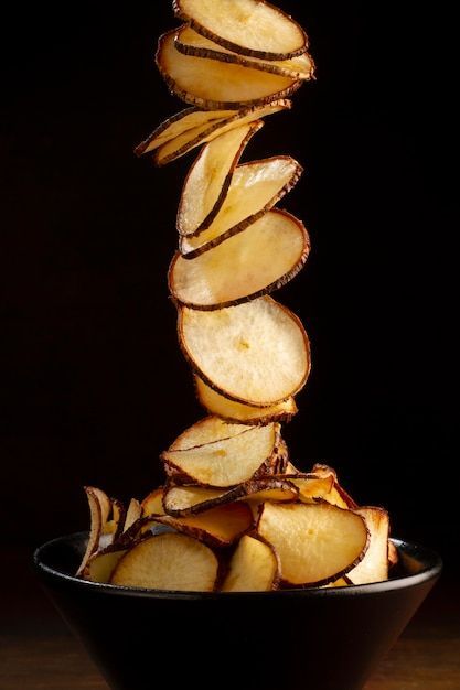 A stack of thin root chips falling into a dark bowl